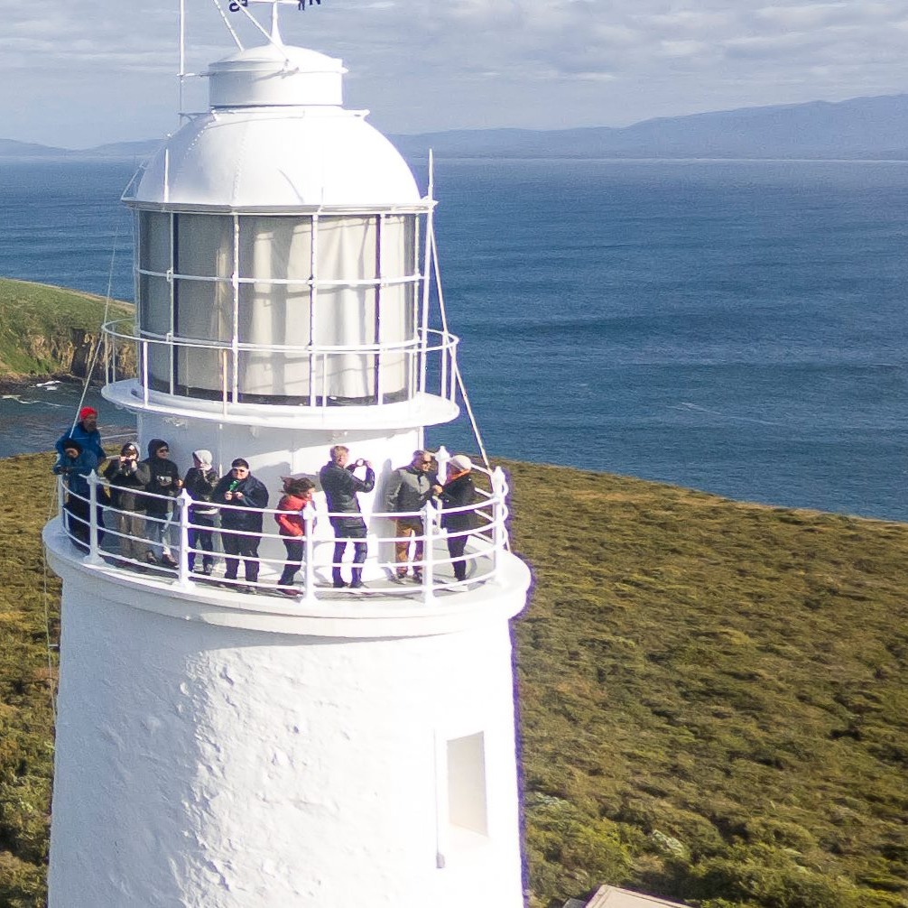 A group of people standing at the top of a lighthouse taking photos of the bay.